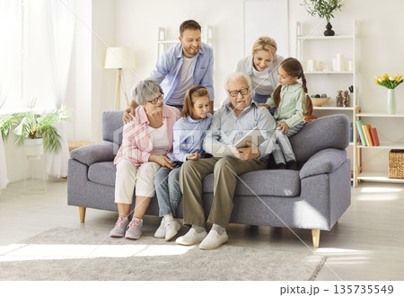Large Family Sitting Together on Couch at Home Enjoying a Photo Album 135735549