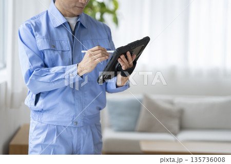 タブレットに入力する作業服を着たの男性の手元 135736008