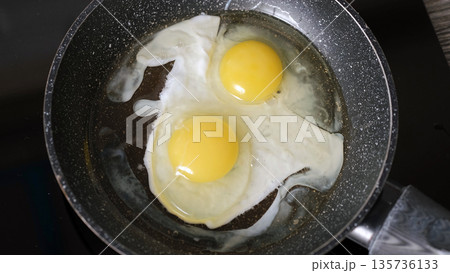 Cracking fresh eggs frying in a hot pan, top view. Morning cooking and breakfast preparation concept  135736133