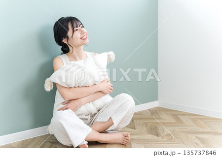 自宅のリビングでクッションを抱きながらくつろぐ笑顔の若いアジア人女性 自宅のリビングでクッションを抱きながらくつろぐ笑顔の若いアジア人女性 135737846