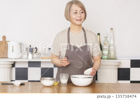 キッチンでアメリカンワッフルを焼くシニア女性 キッチンでアメリカンワッフルを焼くシニア女性 135738474