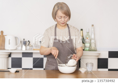 キッチンでアメリカンワッフルを焼くシニア女性 キッチンでアメリカンワッフルを焼くシニア女性 135738492