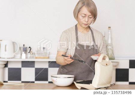 キッチンでアメリカンワッフルを焼くシニア女性 キッチンでアメリカンワッフルを焼くシニア女性 135738496