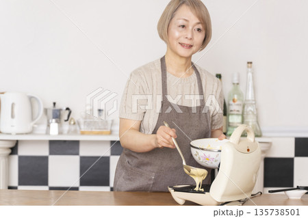 キッチンでアメリカンワッフルを焼くシニア女性 キッチンでアメリカンワッフルを焼くシニア女性 135738501