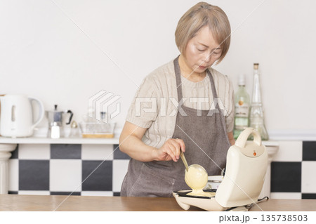 キッチンでアメリカンワッフルを焼くシニア女性 135738503
