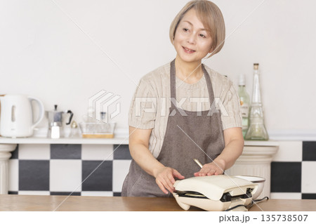 キッチンでアメリカンワッフルを焼くシニア女性 135738507