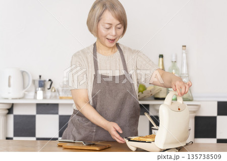 キッチンでアメリカンワッフルを焼くシニア女性 135738509
