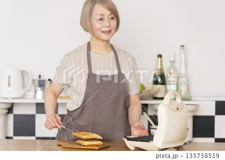 キッチンでアメリカンワッフルを焼くシニア女性 135738519