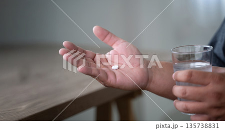 man hand holds a white pill or capsule and a glass of water at home, eating vitamin on time, medicine daily vitamins ginseng or calcium support health, wellness, health and care. 135738831