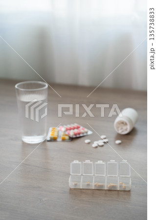Flat lay of medicines with water glass and pill organizer on table, daily medication schedule, healthcare treatment, dosage planning, copy space background. Flat lay of medicines with water glass and pill organizer on table, daily medication schedule, healthcare treatment, dosage planning, copy space background. 135738833
