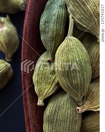 Macro of Green Cardamom Pods in Wooden Spoon on Black Background 135741017