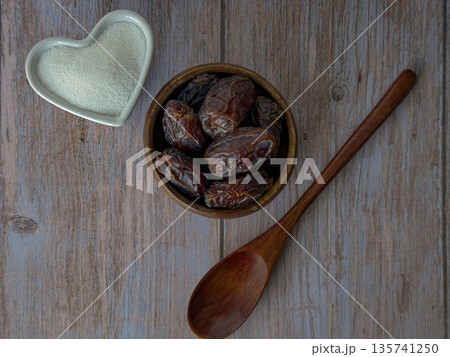 Dried Dates in Wooden Bowl with Spoon and Cane Sugar Heart on Rustic Table Dried Dates in Wooden Bowl with Spoon and Cane Sugar Heart on Rustic Table 135741250