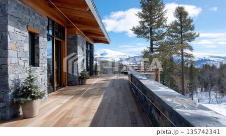 Modern alpine cabin with schist stone wall and wood deck overlooking snowy mountains. 135742341