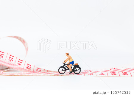 Miniature Cyclist Riding Bicycle on Measuring Tape Miniature Cyclist Riding Bicycle on Measuring Tape 135742533