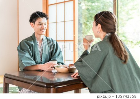 庭の景色が見える旅館の和室でお茶を飲む浴衣姿のカップル,夫婦 135742559