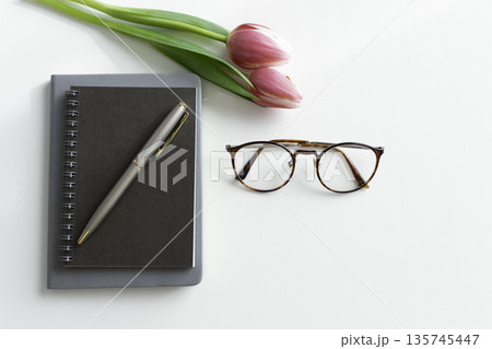 白背景のデスクにチューリップとノートと眼鏡のフラットレイ（コピースペース） 135745447