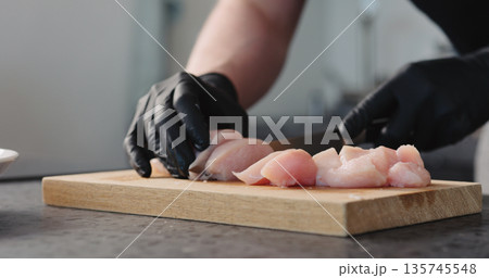 Man hands in black gloves cutting chicken fillet on oak board Man hands in black gloves cutting chicken fillet on oak board 135745548