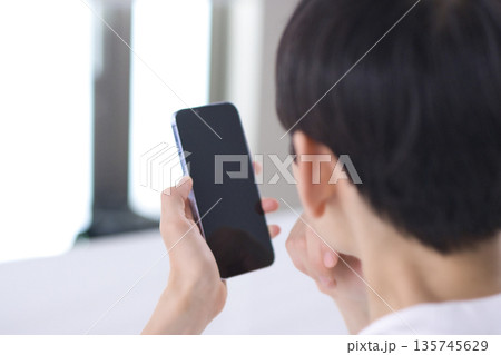 リビングでスマホを見る若い男性の後ろ姿 リビングでスマホを見る若い男性の後ろ姿 135745629
