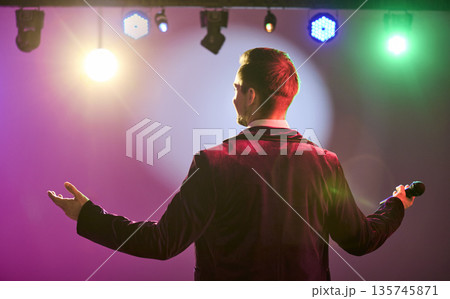 Showman with microphone on stage under colorful lights, back view, open arms 135745871