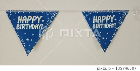 A blue banner with stars and the words Happy Birthday! is hanging on a wall 135746507