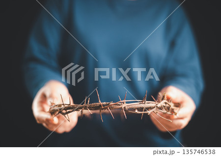 Hands holding a crown of thorns toward the viewer, dark background, dramatic light, shallow depth of field, symbolizing crucifixion, sacrifice, Good Friday, Holy Week, Easter and Christian faith. 135746538