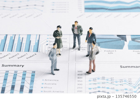 Miniature business team standing on printed financial reports with charts and summary tables, discussing performance metrics, sales trends and strategy for corporate planning and analytics. Miniature business team standing on printed financial reports with charts and summary tables, discussing performance metrics, sales trends and strategy for corporate planning and analytics. 135746550