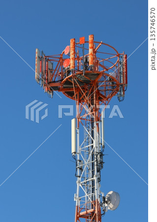 The upper portion of a telecommunications tower rising against a clear, cloudless blue sky. 135746570