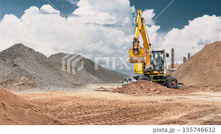A wheeled excavator works at a construction site, moving sand for construction work, surrounded by piles of building materials 135746632