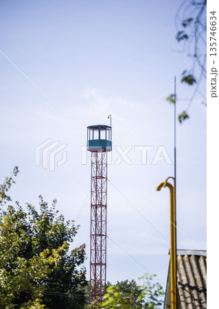 A tall watchtower rises above the trees under a clear blue sky. It serves as a lookout point, providing a view of the surrounding area A tall watchtower rises above the trees under a clear blue sky. It serves as a lookout point, providing a view of the surrounding area 135746634