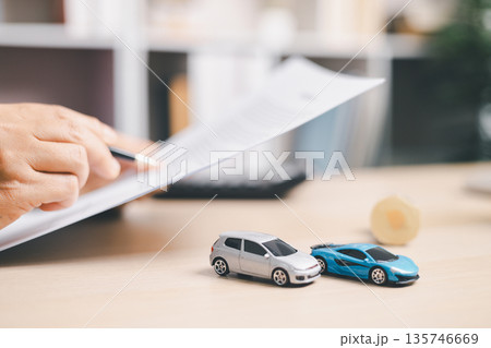 Person signing auto loan agreement on clipboard with car keys and calculator on desk, completing vehicle purchase paperwork, financing approval, insurance details and budget planning. 135746669