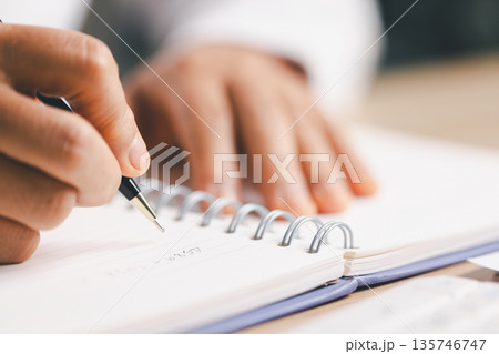 Business person taking notes in a spiral notebook beside a laptop and financial charts, planning strategy, budgeting and reporting for corporate analysis, meeting prep and productivity. Business person taking notes in a spiral notebook beside a laptop and financial charts, planning strategy, budgeting and reporting for corporate analysis, meeting prep and productivity. 135746747