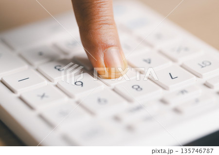 Macro close-up of a finger pressing white calculator keys, performing quick calculations for budgeting, accounting, tax and expense tracking in office or home finance, soft light, shallow focus. Macro close-up of a finger pressing white calculator keys, performing quick calculations for budgeting, accounting, tax and expense tracking in office or home finance, soft light, shallow focus. 135746787