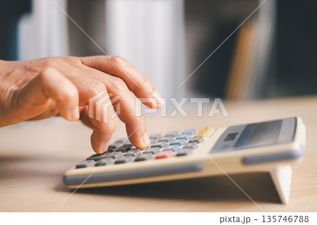 Close-up hand pressing a calculator on a wooden desk in an office, calculating costs for budgeting, accounting, tax, payroll and financial planning in a modern workplace, soft light. 135746788