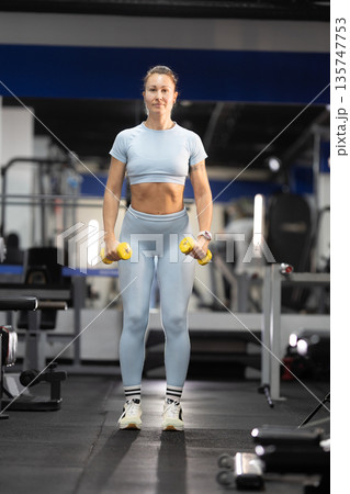 Woman holding dumbbells performing workout in gym Woman holding dumbbells performing workout in gym 135747753