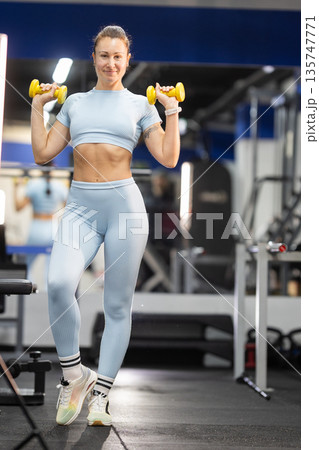 Woman exercising with dumbbells, training arms in gym Woman exercising with dumbbells, training arms in gym 135747771