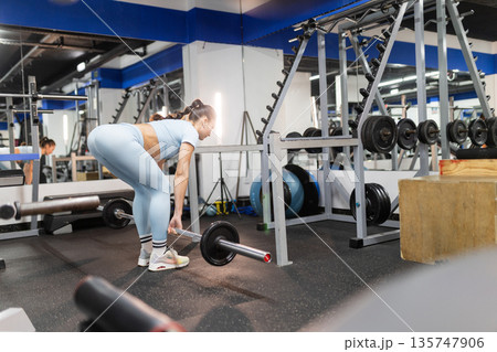Woman preparing to lift barbell during fitness workout in gym 135747906