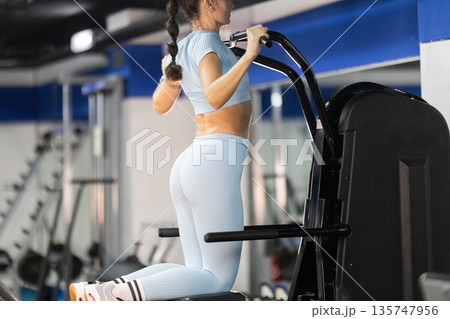 Woman training in gym using assisted pull-up machine Woman training in gym using assisted pull-up machine 135747956