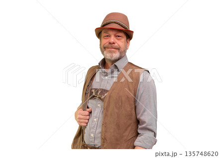 A man aged 50 55 wearing a traditional Tyrolean waistcoat and hat poses against a white background. A man aged 50 55 wearing a traditional Tyrolean waistcoat and hat poses against a white background. 135748620