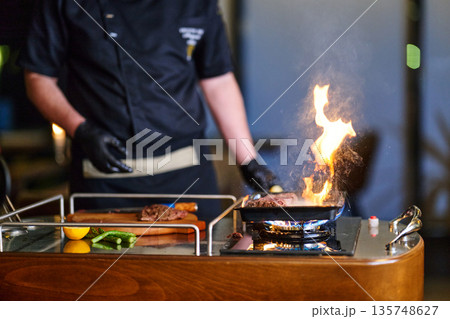 Professional Chef Grilling Tender Steak On Open Flame In Modern Kitchen Studio During Live Cooking Professional Chef Grilling Tender Steak On Open Flame In Modern Kitchen Studio During Live Cooking 135748627