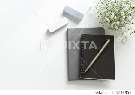 白背景のデスクにノートとペンと消しゴムとかすみ草のフラットレイ（コピースペース） 135748953