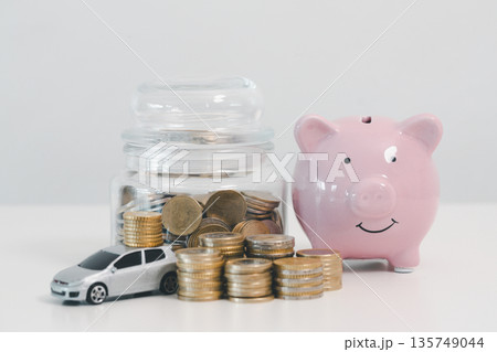 Pink piggy bank with coin jar, stacked coins and toy car on white background, symbolizing car savings, down payment goals, auto loan budgeting and personal finance planning. 135749044