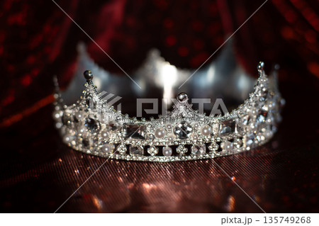 White crown with crystals, diamonds on dark red sparkle background. White crown with crystals, diamonds on dark red sparkle background. 135749268