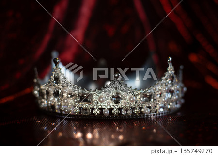 White crown with crystals, diamonds on dark red sparkle background. White crown with crystals, diamonds on dark red sparkle background. 135749270