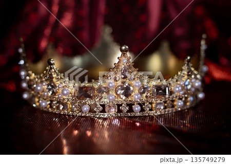 Ancient golden medieval crown with gemstones on sparkle red background. 135749279