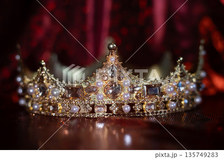 Ancient golden medieval crown with gemstones on sparkle red background. 135749283