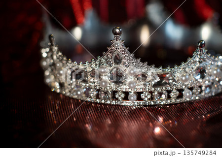White crown with crystals, diamonds on dark red sparkle background. White crown with crystals, diamonds on dark red sparkle background. 135749284