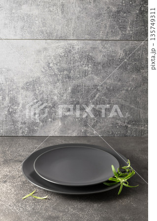 Empty round black plates with rosemary on a grey stone background. Empty round black plates with rosemary on a grey stone background. 135749311