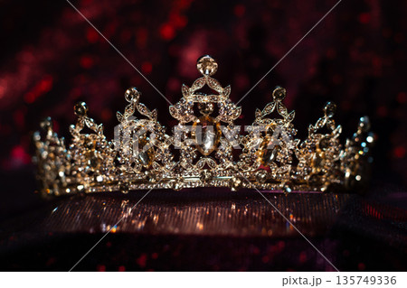 Golden yellow crown with citrines, gemstones on dark sparkle red background. Golden yellow crown with citrines, gemstones on dark sparkle red background. 135749336
