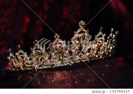 Golden yellow crown with citrines, gemstones on dark sparkle red background. 135749337