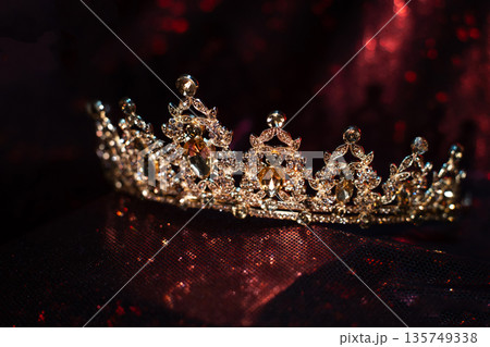 Golden yellow crown with citrines, gemstones on dark sparkle red background. 135749338